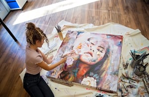 Damitra girl in tan shirt and black pants painting a portrait on the floor in well lit room